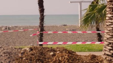 Kapalı karantina bölgesi. Sokakta palmiye ağaçları ve deniz olan uyarı bandı. Kazı ve inşaat alanının yakınındaki şeritli kırmızı ve beyaz kurdele. Onarım çalışmaları sırasında geçici engeller.