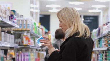 Kadın kozmetik ürünlerini dükkanda seçiyor. Siyah paltolu güzel sarışın kadın elinde bir kutu tutuyordu. Yandan bak. Kişisel bakım ürünleri ve modern kozmetoloji.