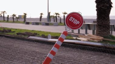 İnşaat alanının arka planında palmiye ağaçları ve deniz kenarlarında gezinen dur tabelası. İşaret rüzgarla savrulur ya da vandallar tarafından kırılır.