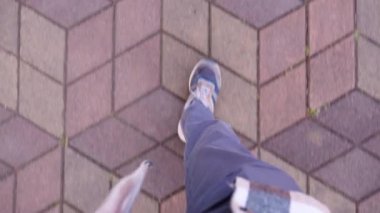 Kotlu ve beyaz spor ayakkabılı bir adam kaldırım levhalarında yürüyor. Birinci şahıs bakış açısıyla insan yürüme ya da sokakta şort ve spor ayakkabılarla gezinme görüntüsü
