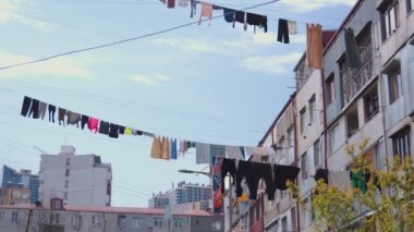 Mavi arka plandaki binalar arasında ipte asılı çok renkli giysiler. Şehirde ipte asılı duran temiz tekstil ürünlerini yıkadım. Çamaşırları kurutuyorum. Yoksulluk Evi.