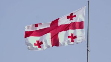 Gürcistan 'ın ulusal bayrağının yakın çekimi mavi gökyüzüne karşı kopyalanmış uzayla dalgalanıyor. Uluslararası ilişkiler kavramı. Gürcistan bayrağı açık, mavi gökyüzünün arka planında rüzgarda dalgalanıyor. Yavaş çekim