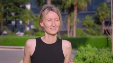 Siyah bluzlu genç kız güneşli bir günde tropikal parkta palmiye ağaçlarıyla koşuyor. Sağlık sporu kadın spor konsepti gündoğumu koşucusu. Modern parkta palmiye ağaçlarının arasında