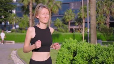 Siyah bluzlu genç kız güneşli bir günde tropikal parkta palmiye ağaçlarıyla koşuyor. Sağlık sporu kadın spor konsepti gündoğumu koşucusu. Modern parkta palmiye ağaçlarının arasında