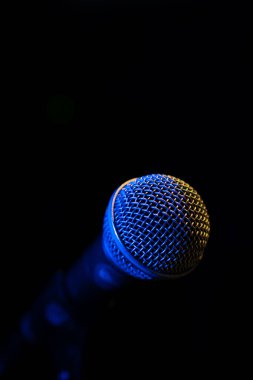 Bir müzik stüdyosunda, karanlıkta bir konserde, arka fonda mavi ışık olan bir mikrofonun yakın çekimi, kopyalama uzayı. Dikey fotoğraf