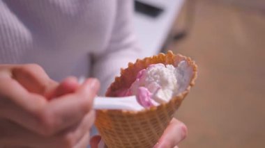 Genç bir kadının elleri yakın çekim plastik kaşık alıyor waffle külahı alıyor dondurma yiyor ve açık havada parkta yiyor..