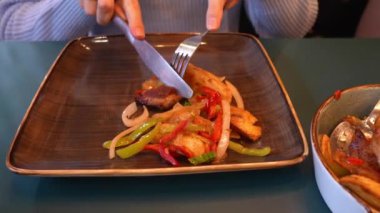 Geleneksel Gürcistan tarifi Ojakhuri domuz eti ve patatesle yakın plan. Çatal ve bıçakla et kesen kadın elleri tabakta patates kızartması ve üst tabakta Ojakhuri. Gürcistan mutfağı,