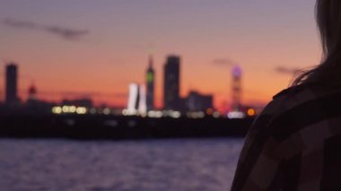 Bulutlu, turuncu gökyüzü Batumi, Adjara, Georgia 'da gün batımı ve şehir sınırı. Ön planda odak dışı kadın silueti var. Şehre uzaktan bakıyor..