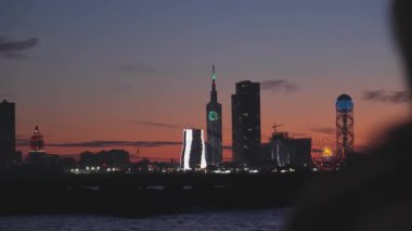 Bulutlu, turuncu gökyüzü Batumi, Adjara, Georgia 'da gün batımı ve şehir sınırı. Önplanda, kadın silueti odak dışı, elleriyle Serda 'yı şekillendiriyor, şehre olan aşkını gösteriyor..