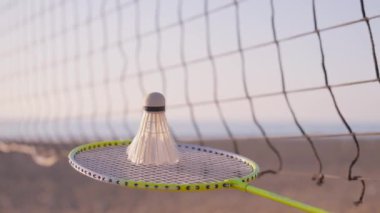 Badminton raketi ve kumsalda bir mekik, ağ ve deniz altyapısı. Sportif yaşam tarzı. Yaz tatili ve spor. Badminton ekipmanları, raketler ve açık hava sporları.