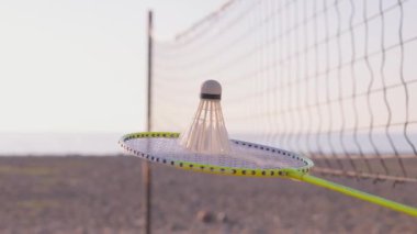Badminton raketi ve kumsalda bir mekik, ağ ve deniz altyapısı. Sportif yaşam tarzı. Yaz tatili ve spor. Badminton ekipmanları, raketler ve açık hava sporları.