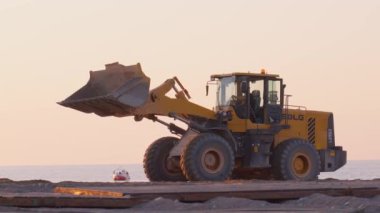 Batumi, Gürcistan - 2 Mayıs 2024: Gün batımında deniz kıyısında inşaat alanında çalışan kazıcı, dönen platformdaki kova ve taksiden oluşan ağır inşaat ekipmanıdır..