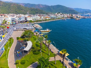 Marmaris, Türkiye - 9 Eylül 2023: Güneşli bir günde Marmaris kentinin evleri, parkları, tekneleri, denizleri ile dağların arka planına bakan insansız hava aracı görüntüsü, Türkiye.