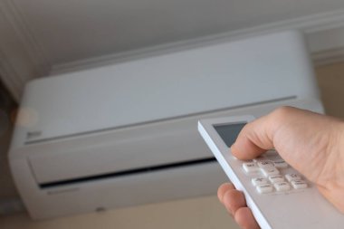 Uzaktan kumandalı bir adamın eli odayı ısıtmak için klimayı açar. Elektrikli ısıtma sistemi. Isıtma mevsimi sonbahar ya da kışın gelmesiyle başlar..