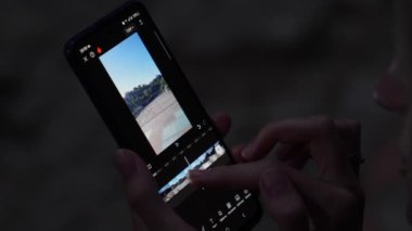 Telefonundaki video düzenleyici yazılımı. Kadın, proje üzerinde çalışırken cep telefonunda video düzenlemesi yapan Ekin içeriği oluşturucusuyla video düzenliyor.