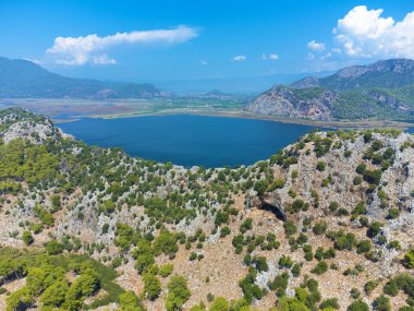 Türkiye 'nin güneşli bir gününde Dalyan Nehri ve Iztuzu Sahili yakınlarındaki dağların insansız hava aracı manzarası. Dağların etrafında bir nehir olan güzel dağ manzarası yaz günü