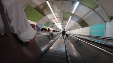 Metro istasyonunda yürüyen merdivenle inen insanlar, hareketli şehir ortamında şehir seyahatleri ve ulaşım dinamikleri sergiliyorlar.