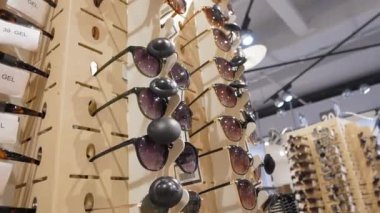 Optik mağazada çeşitli stil ve renklerde modaya uygun güneş gözlüklerinin dönüşümlü görüntüsü, modern göz giysisi sergileniyor