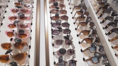 Optik mağazada çeşitli stil ve renklerde modaya uygun güneş gözlüklerinin dönüşümlü görüntüsü, modern göz giysisi sergileniyor