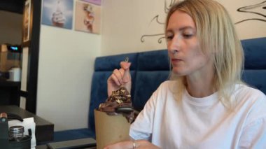 Genç bir kadın yoğun kafede lezzetli tatlı trdelnik 'in keyfini çıkarırken aynı zamanda canlı bir şekilde ekranın dışında biriyle sohbet ediyor ve etrafındaki canlı atmosferin tadını çıkarıyor.