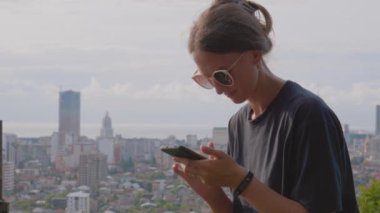 Geniş şehir manzarasının akıllı telefonuyla fotoğraf çeken genç bir kadın. Gürcistan 'ın batısındaki Batumi şehrine tepede yer alır..