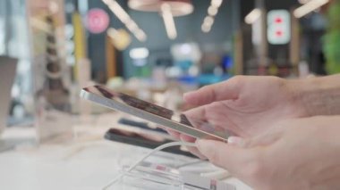 Müşteri akıllı telefonu elinde tutuyor ve elektronik mağazasındaki özellikleri ve uygulamaları karşılaştırıyor. Teknoloji ve iletişim alanındaki kişisel ihtiyaçlarını ve tercihlerini karşılayan mükemmel aygıtı seçiyor.