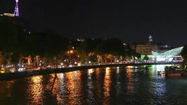 Şehir ışıkları Tiflis, Gürcistan 'da nefes kesici bir gece sahnesi yaratıyor. Barış köprüsü ve hareketli şehir planına karşı yoğun bir trafik var.