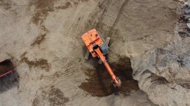 Kazıcı, nehrin yakınındaki inşaat alanında, çöp kamyonuna kum yüklüyor. İnşaat alanında kazıcının çöp kamyonunu yüklerken en tepeden aşağı bakışı. Kazıcı yerde çukur kazıyor.