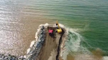Kazıcı ve çöp kamyonu göl ya da deniz kıyısında. Çöp kamyonu toprağa toprak dökerek set ya da yapay kıyı oluşturur. BAtumi, Georgia.