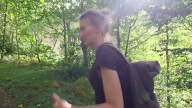 Sırt çantalı iki genç kadın yemyeşil ormanda yürüyor güzel bir yaz günü güneşlenirken doğanın tadını çıkarıyorlar. Turizm gezisi.