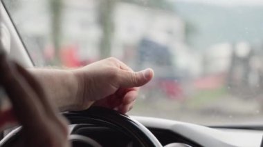 Adam telefonu kulağına dayamış ve diğer eliyle trafikte yön değiştiriyor. Sahne, şehir ortamında dikkatsiz sürüş riskini yakalıyor. Sürücü arabası yakın plan..