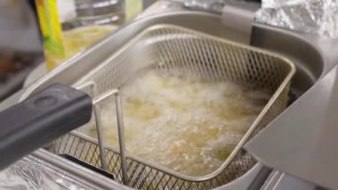 Şef, kızartma makinesinden bir sepet altın kızartma alıyor. Bu süreç profesyonel mutfak ortamında kızartma sanatını vurguluyor