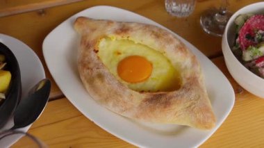 Garson, geleneksel Gürcistan usulü çiğ yumurtalı peynirli ekmek tabağını müşteriler için masaya koyuyor.