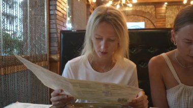 İki beyaz kız arkadaş klasik restoranda ne sipariş edeceklerine karar veriyorlar. Menüyü ellerinde tutuyorlar ve seçenekleri tartışıyorlar..