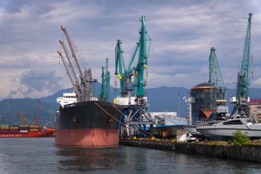 Batumi, Georgia - 24 Temmuz 2024: Yüklenen bir kargo gemisiyle dolu liman, arka planda dağlar. Batumi 'de küresel ticaret ve ticareti gösterir.