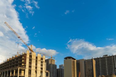 İnşaat vinçleri güneşli bir günde yeni bir apartmanda çalışıyor. Resim, büyüme, gelişme ve ilerleme gibi kavramları çağrıştırır