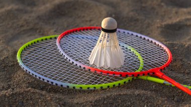 Close-up of two rackets with a shuttlecock on the sand of an open badminton court. Concept of active recreation and recreational sports. clipart