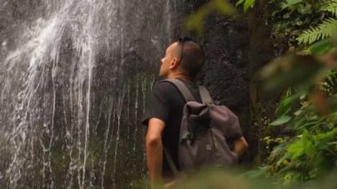 Sırt çantasıyla gezen erkek turist şelalesi yemyeşil yağmur ormanlarına daldırıldı, kendini doğanın güzelliğine ve sükunetine daldırdı.