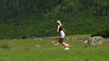 Genç kadın neşeli bir şekilde koşuyor, kollarını açmış, çarpıcı dağ manzarasını kucaklıyor. Sahne, doğada özgürlük ve mutluluk hissini yakalar.