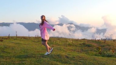 Kadın, kollarını açarak çimenli bir dağın tepesinde duruyor. Etrafını saran bulutların ve dağların güzelliğini kucaklıyor. Dans eder ve hayattan gülümseyerek zevk alır. Yavaş çekim