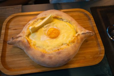 Ajarian tarzı ahşap bir tepside Khachapuri 'ye yakın çekim. Geleneksel Gürcistan yemekleri içinde peynir, yumurta ve tereyağı bulunan tekne şeklinde ekmeklerden oluşur..
