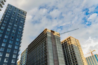 Modern apartman binaları, cam balkonlar, mavi gökyüzünün altında beyaz bulutlar, çağdaş şehir mimarisini gözler önüne seriyor.