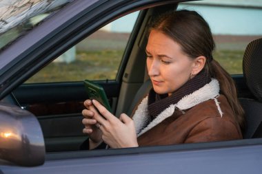 Arabadaki endişeli kadın telefonundan şok edici haberler okuyor. Bilgiyi yönetirken karışık duygular hissediyor.