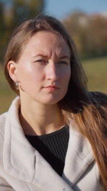 Genç bir kadın güneşli bir sonbahar gününde parkta bankta oturuyor. Elleriyle kıpırdıyor ve düşüncelere dalmış gibi görünüyor. dikey video