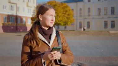 Kahverengi ceketli, üzüntüsünü ve endişelerini ifade eden genç bir kadın kaybolmuş ve telefonundaki haritalardan yolunu bulamıyor. Şehir çevresi duygusal mücadelesini yoğunlaştırıyor, yalnızlık üzüntüsünü.