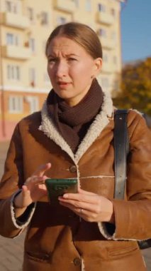 Kahverengi ceketli, üzüntüsünü ve endişelerini ifade eden genç bir kadın kaybolmuş ve telefonundaki haritalardan yolunu bulamıyor. Şehir çevresi duygusal mücadelesini yoğunlaştırıyor, yalnızlık üzüntüsünü.