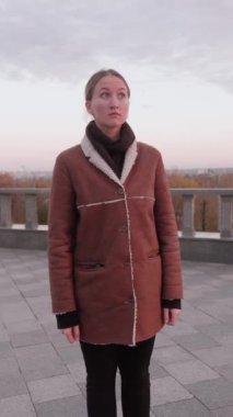 Genç bir kadın hayal kırıklığını ve rahatsızlığını ifade ediyor. Duygularını dışa vuruyor. Stres, endişe ve üzüntü duyguları, şehir sonbahar ortamındaki sorunlu durumunu yansıtıyor. dikey video