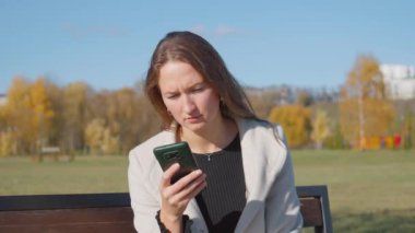 Parktaki bankta otururken telefonu kullanan genç ve güzel bir kadın. O, yanında uzun ceket ve bir bardak kahve giyer. Sonbahar Şehir Parkı.