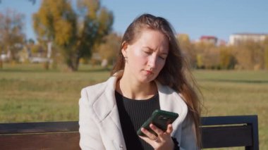 Parktaki bankta otururken telefonu kullanan genç ve güzel bir kadın. O, yanında uzun ceket ve bir bardak kahve giyer. Sonbahar Şehir Parkı.