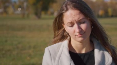 Uzun kahverengi saçlı genç bir kadın parktaki bankta oturur, üzüntü ve hayal kırıklığını ifade eder. Yalnızlık ve kaygı duyguları onun sorunlu durumunu yansıtıyor.